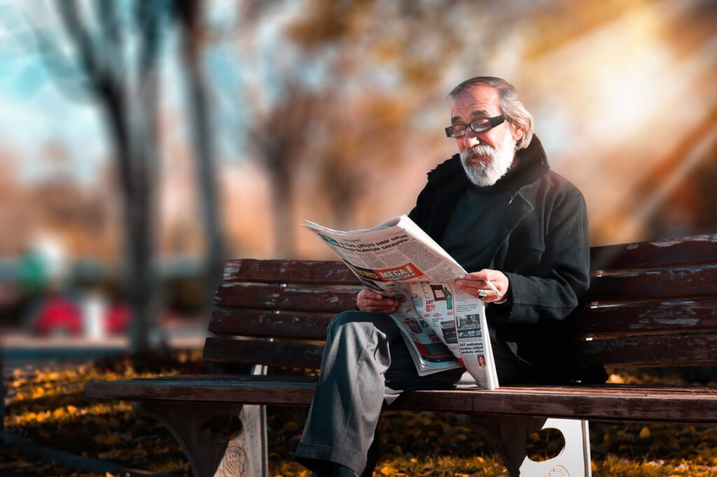 Man on bench reading newspaper. Imahe by Hasan Albari